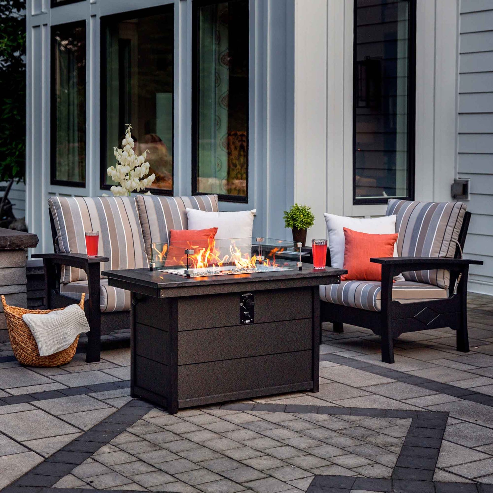 Striped cushion poly patio loveseat and chair flanking a lit rectangular fire pit table on a paver patio