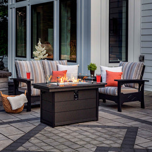 Poly patio loveseat and chair with gray striped cushions beside a glowing fire pit table at dusk
