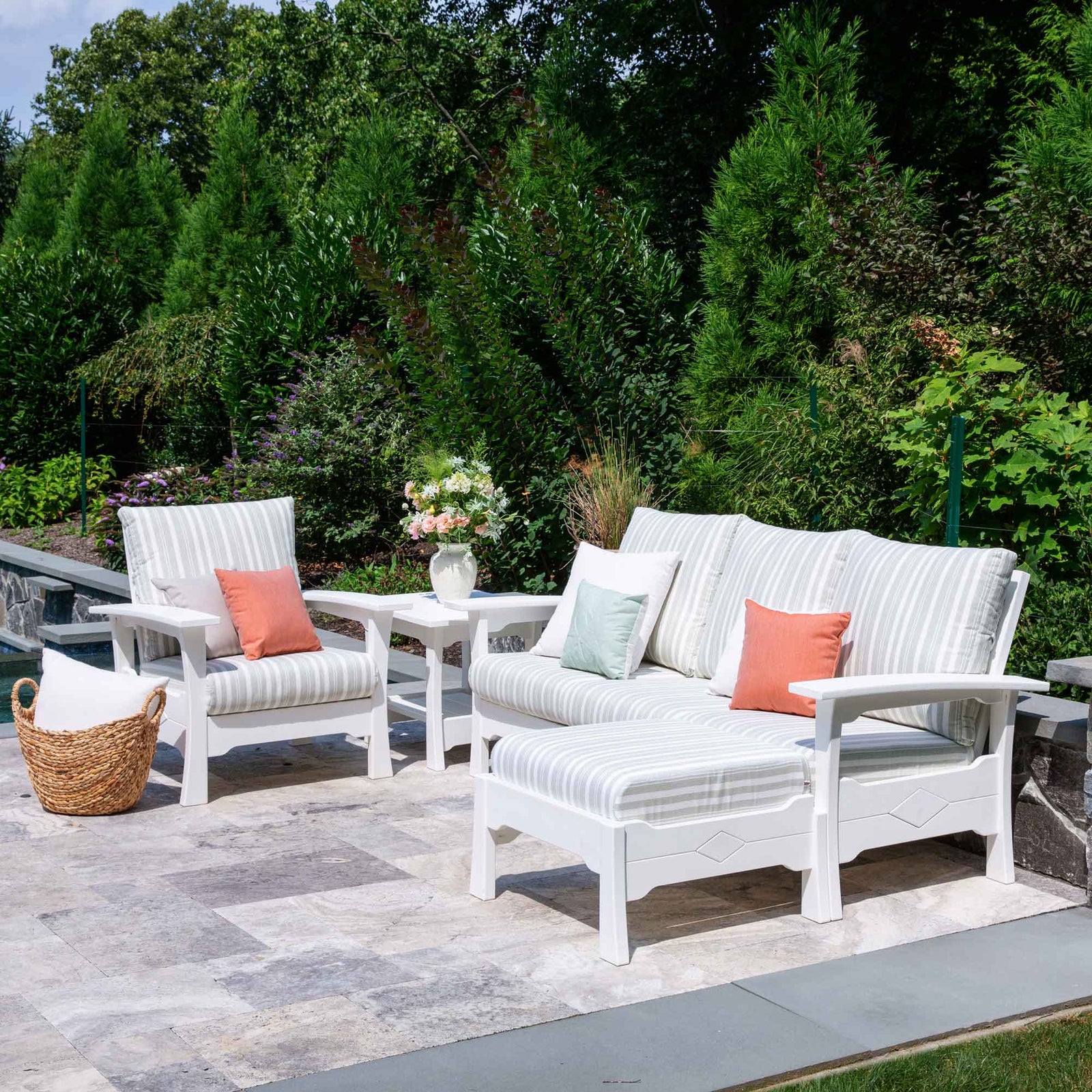 White poly patio sofa, chair and ottoman with soft striped cushions and a side table by a pool