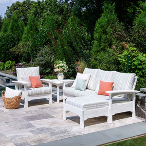 White poly patio sofa, chair and ottoman with soft striped cushions and a side table by a pool