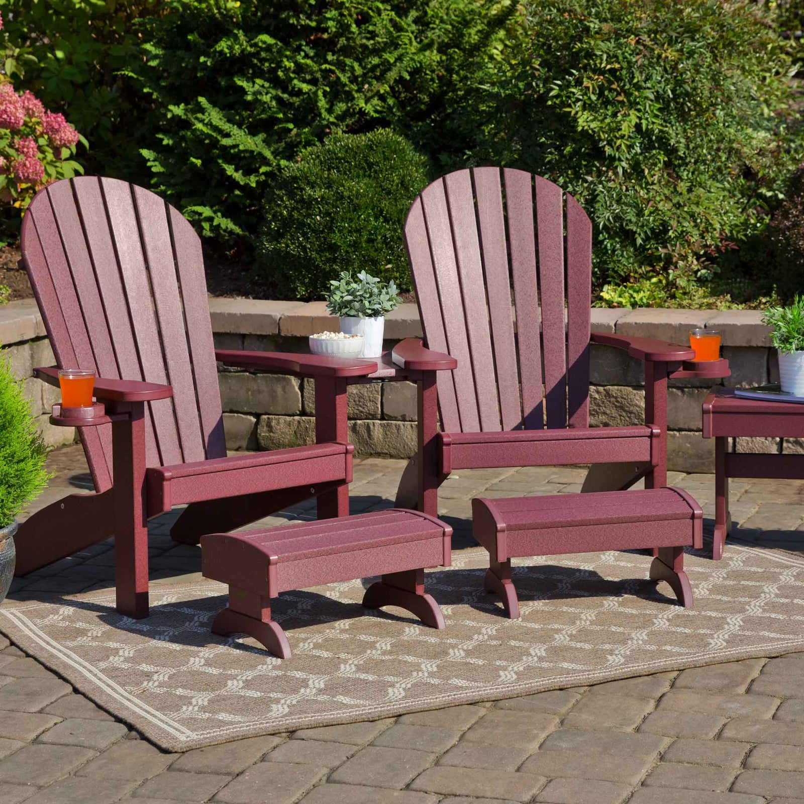 Cherrywood red poly Adirondack chairs with cup holders, matching footstools and a shared settee table on a patio
