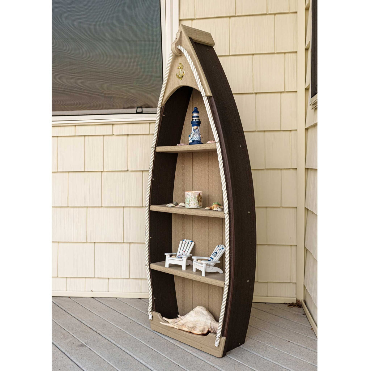 Brown and tan boat shaped shelf on a porch, holding a lighthouse figurine, books and mini Adirondack chairs