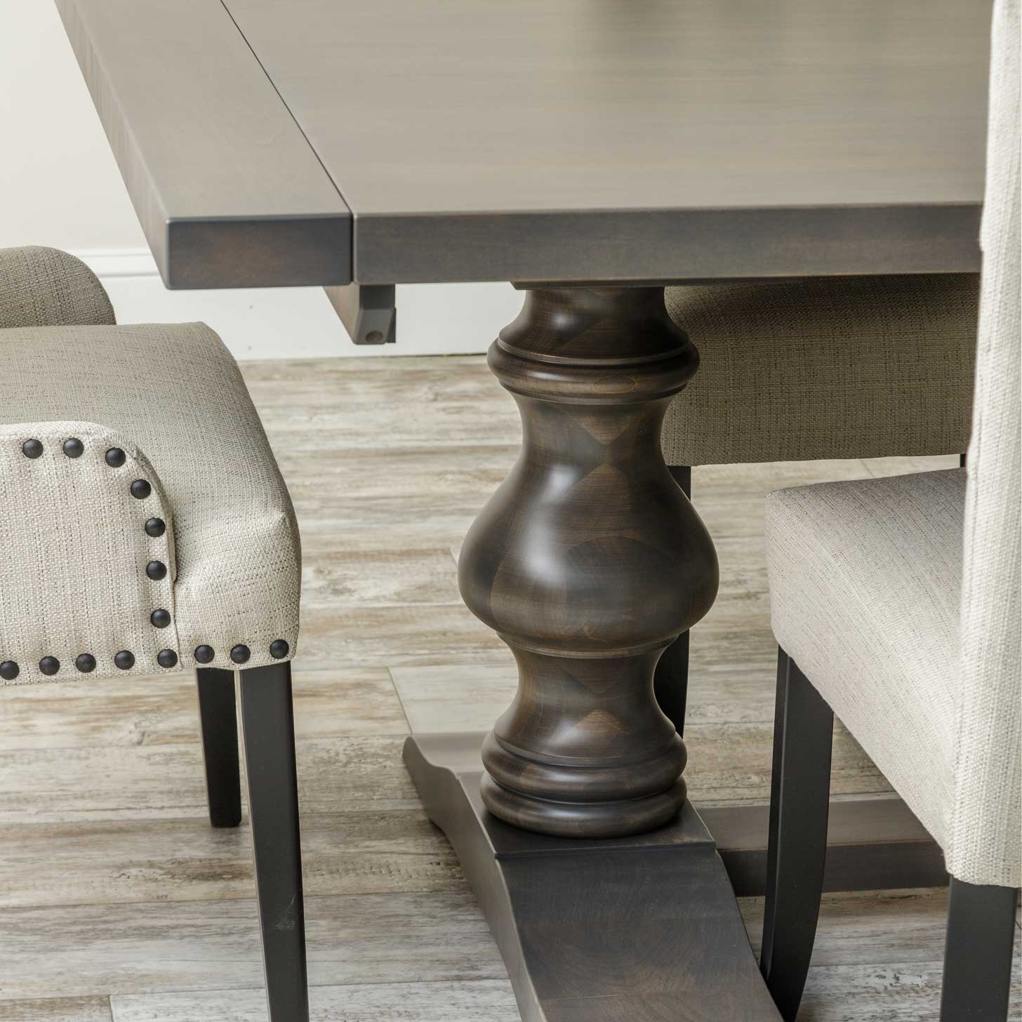 Alana trestle dining table in weathered gray with six cream upholstered nailhead chairs and a matching china cabinet behind