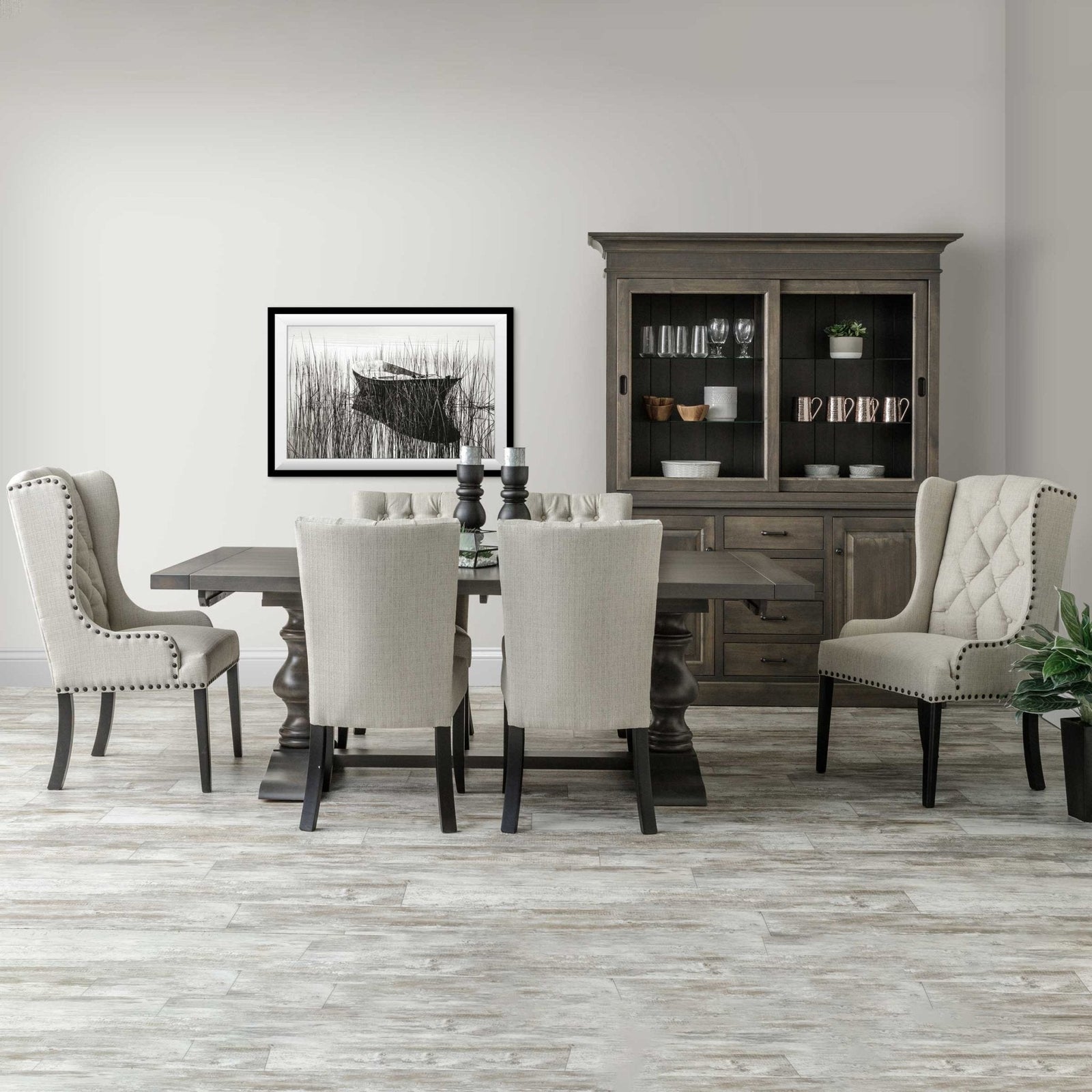 Alana trestle dining table in weathered gray with six cream upholstered nailhead chairs and a matching china cabinet behind