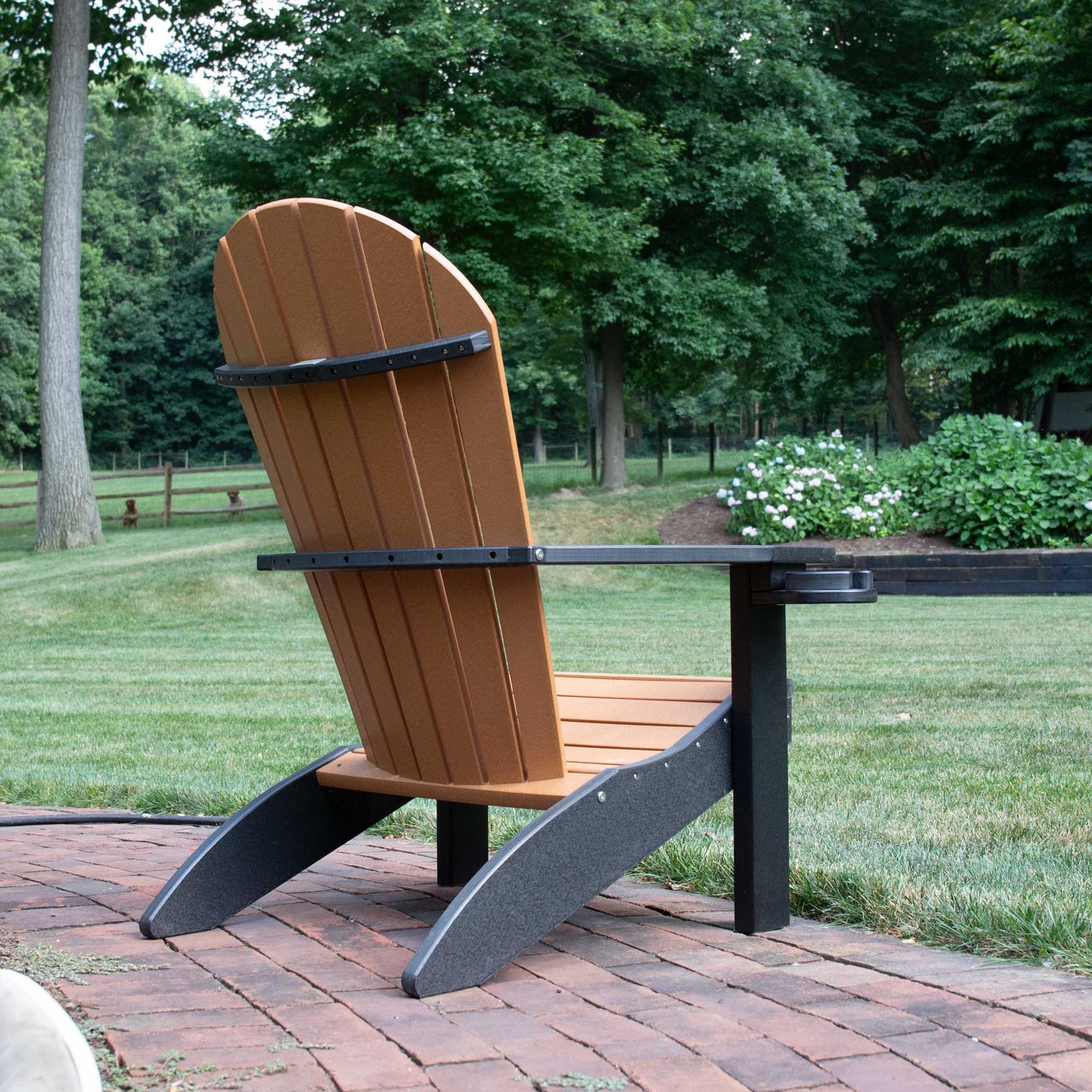 Gray and driftwood poly Adirondack chair with a striped orange pillow on a flagstone patio beside blooming roses
