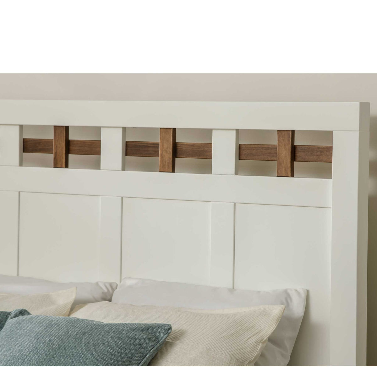 Detail of the white lattice headboard top rail with brown wood accents above a bed dressed in white and blue