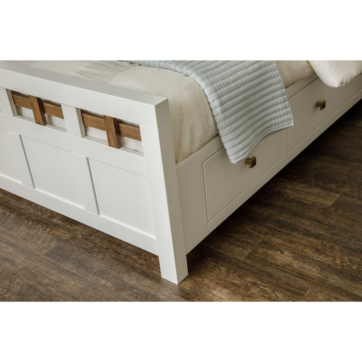 Corner view of the white storage bed footboard with lattice accents and two brass-knob drawers under the mattress