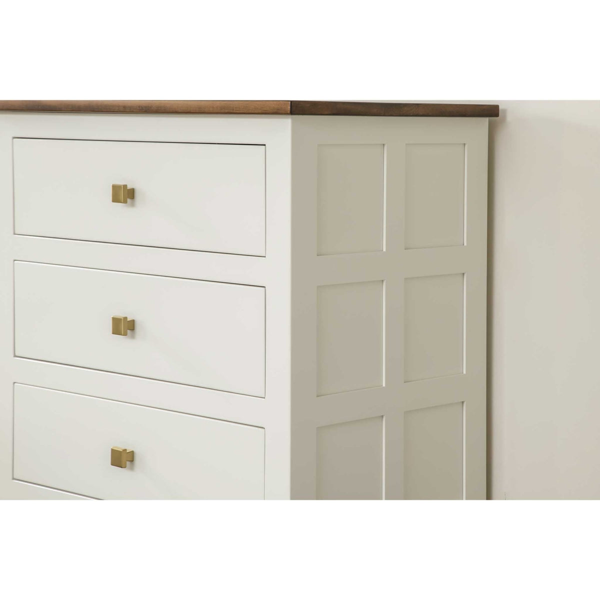 Close view of the cream dresser side panel grid and three drawer fronts with square brass hardware