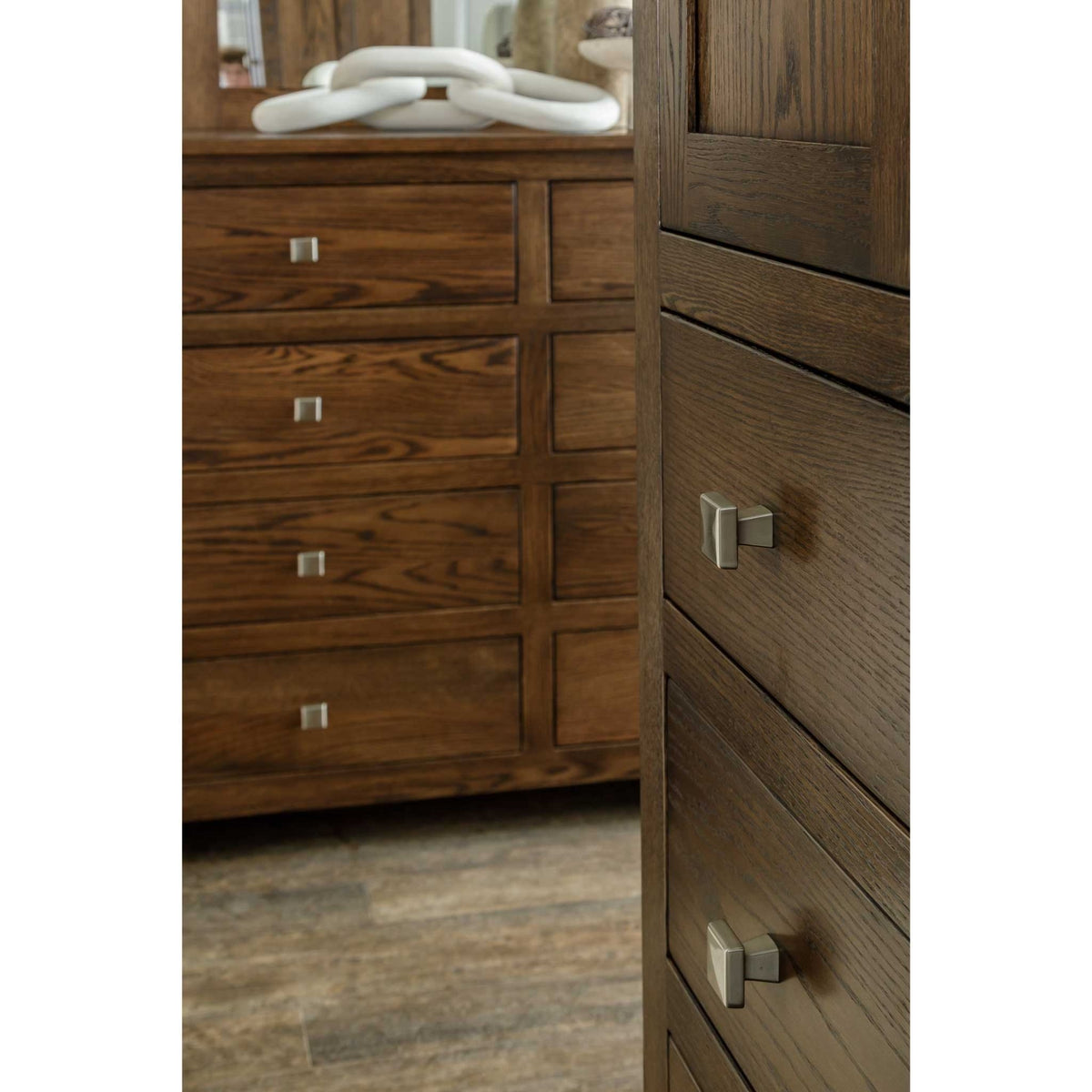 Nickel square knobs on a dark oak chest in the foreground with a matching oak dresser blurred behind