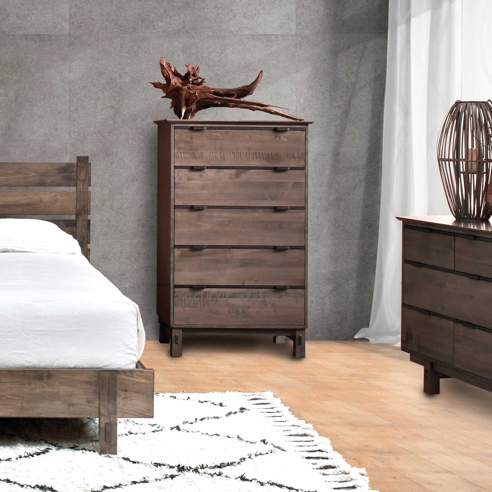 Rustic five drawer chest of drawers in weathered brown wood with black bar pulls, styled in a gray modern bedroom with bed