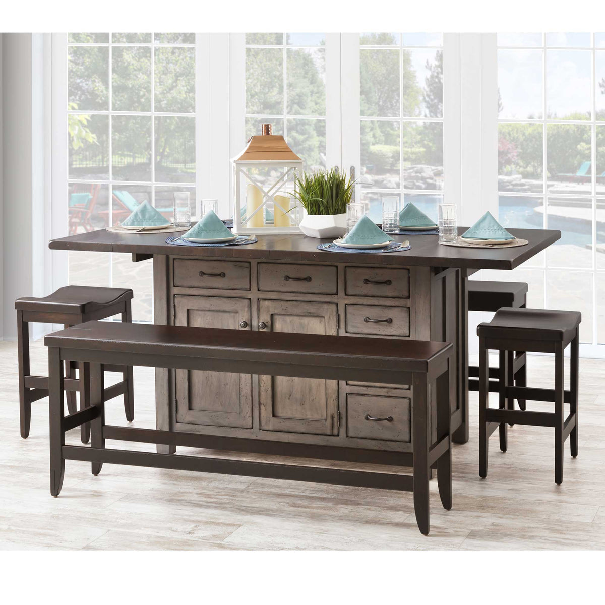 Two-tone kitchen island with weathered gray base, dark drop leaf top, counter bench and two saddle stools by a window