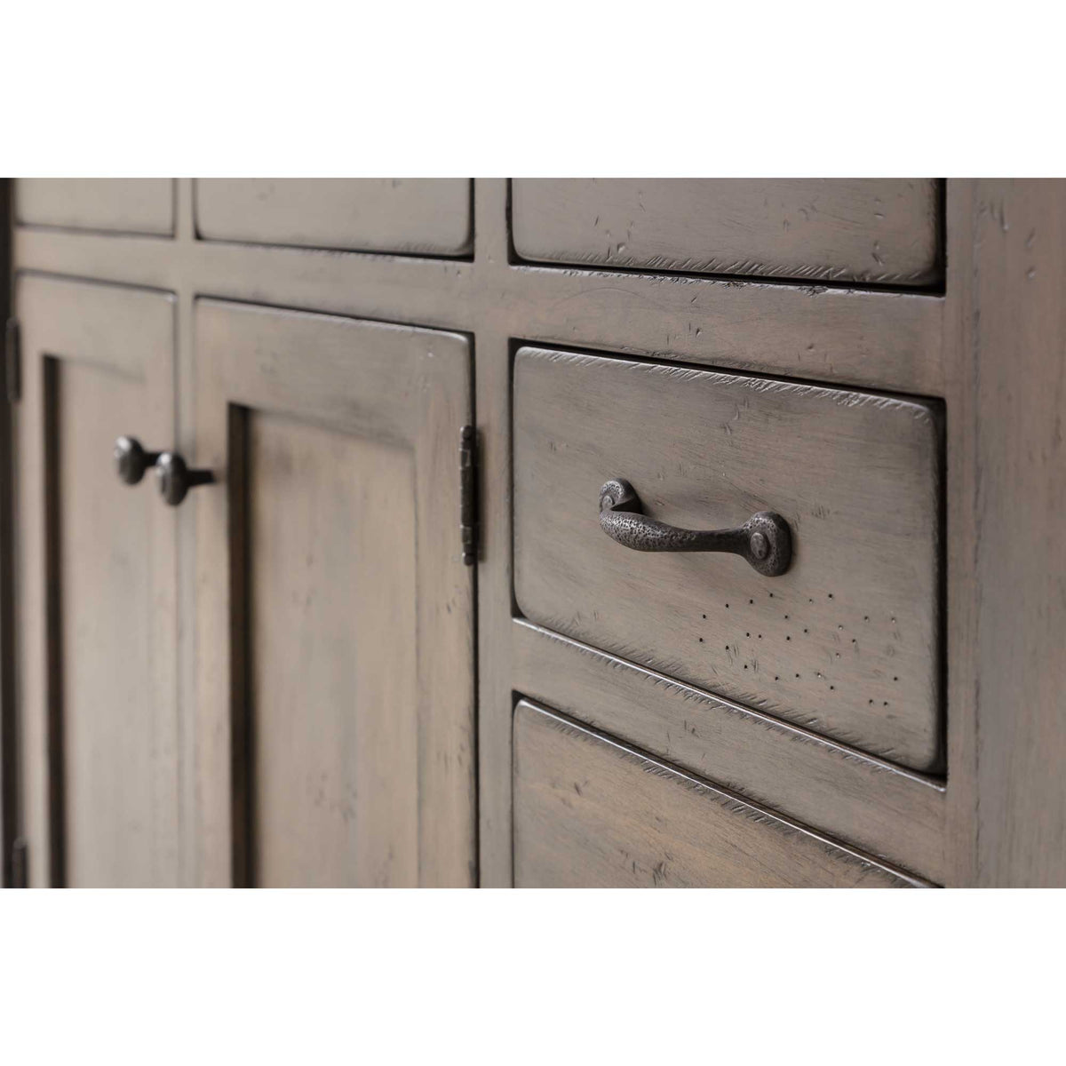 Detail of distressed gray cabinet doors and drawers with hammered black iron pulls and knobs on a kitchen island