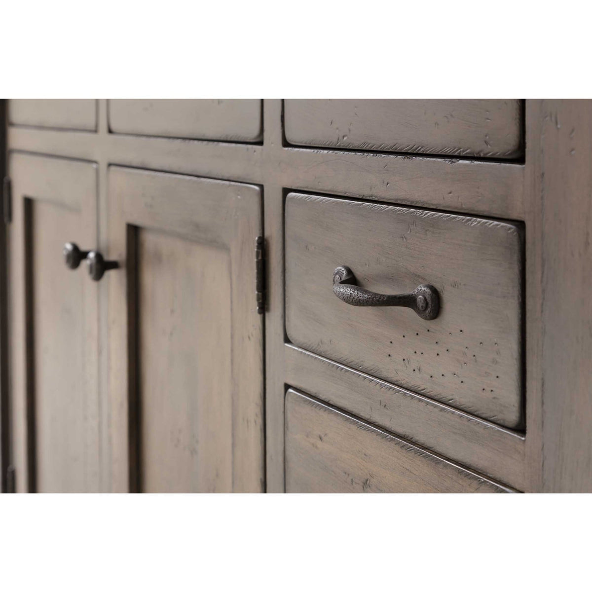 Close view of hammered iron hardware on the distressed gray raised panel doors and drawers of a kitchen island