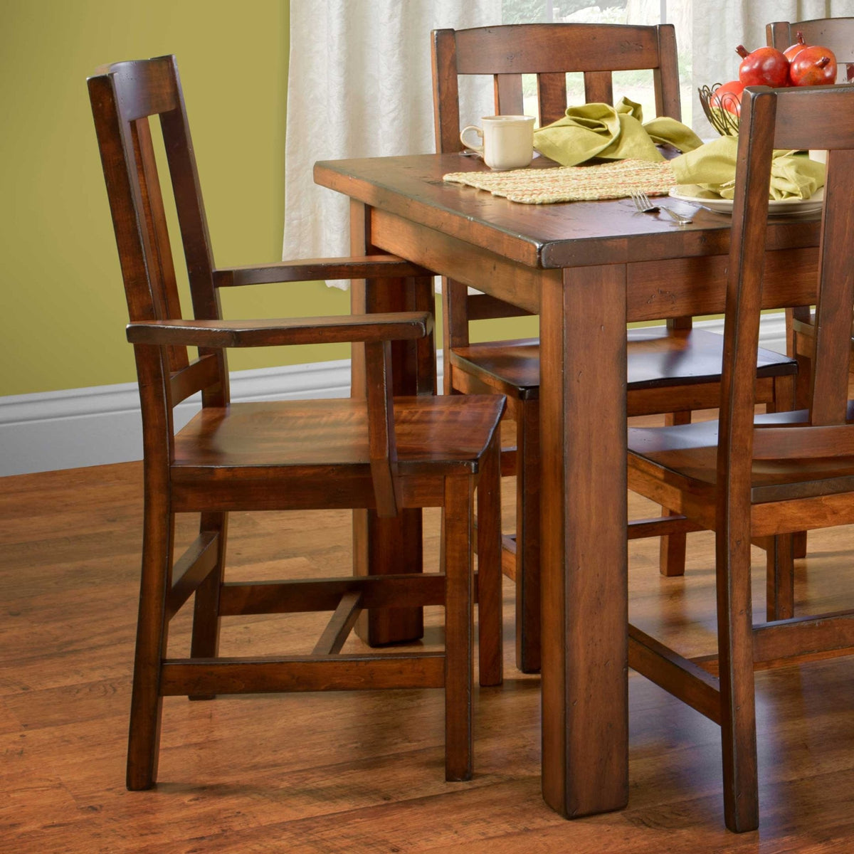 Cherry arm chair with slat back and wood seat pulled beside the rustic dining table in a green room