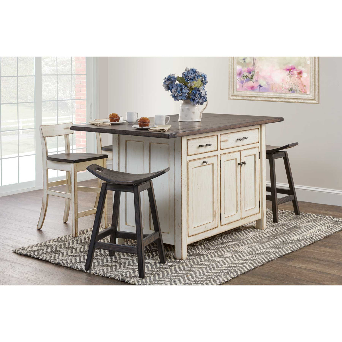 Distressed cream kitchen island set with brown top, saddle stools and a bar chair by a bright window