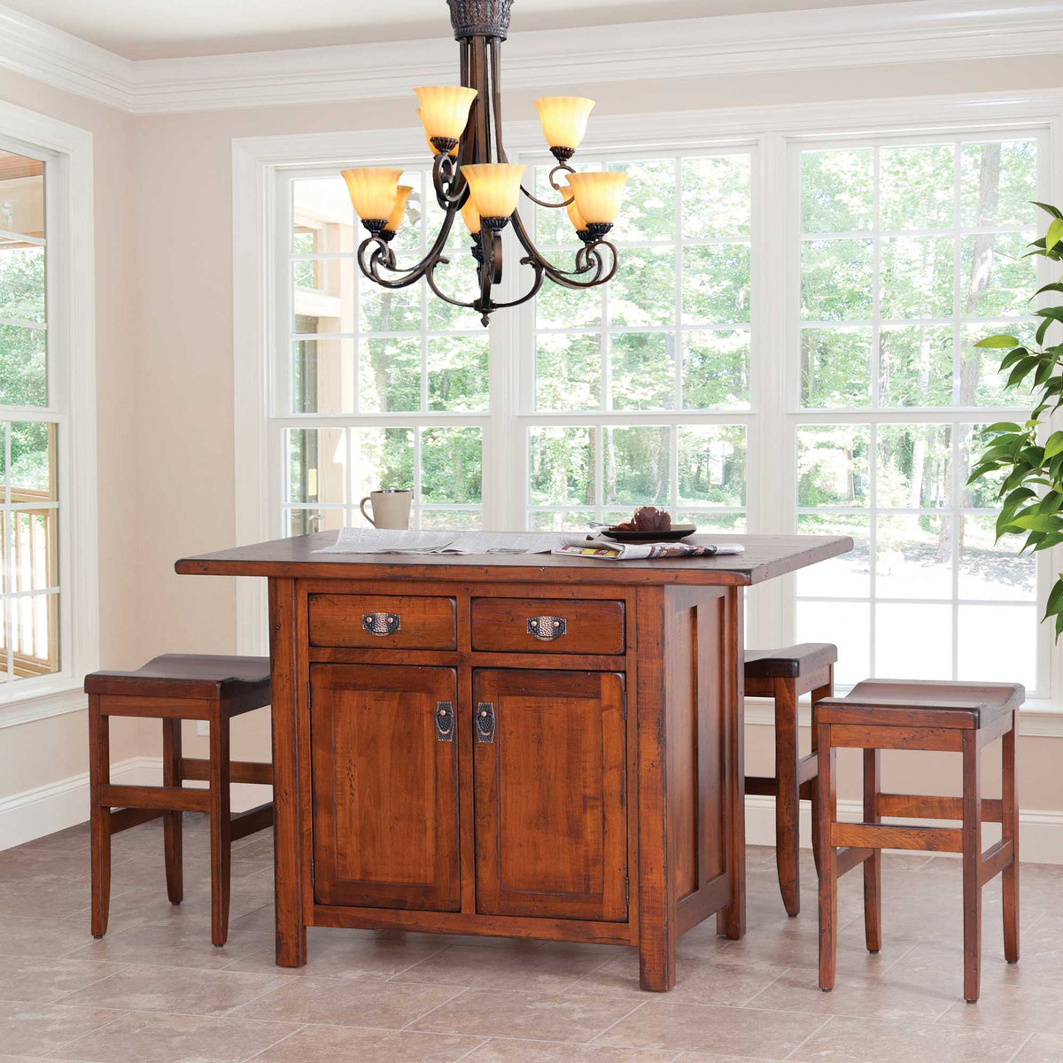Cherry kitchen island set for four with two saddle stools under a chandelier in a window-lined breakfast room