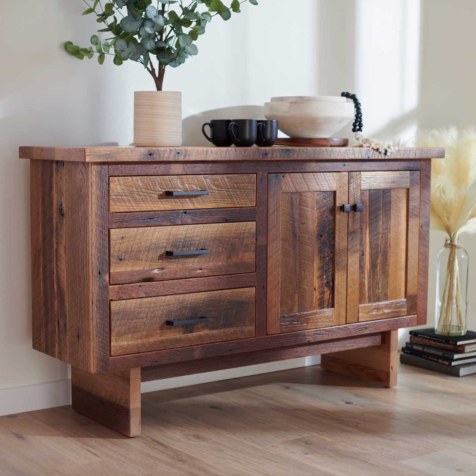 Rustic reclaimed wood sideboard buffet with three drawers and two cabinet doors styled with mugs and a bowl