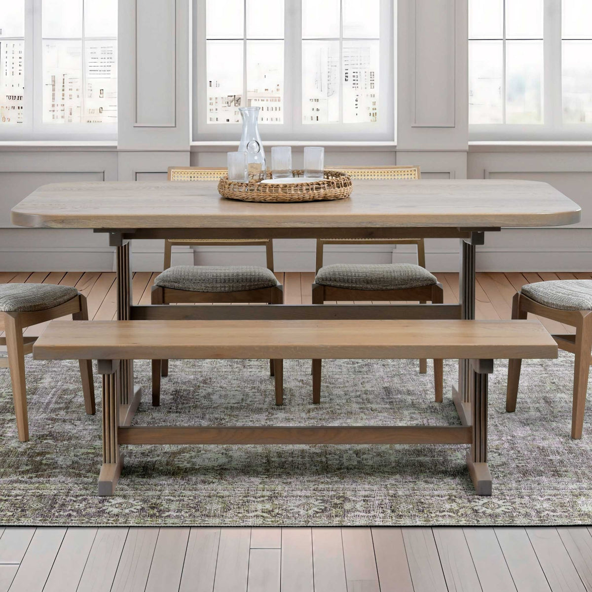 Solid top trestle table with bench and upholstered chairs in a white room with large windows