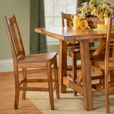 Warm maple bar chair with slat back and wood seat beside a counter height trestle table set with yellow mugs