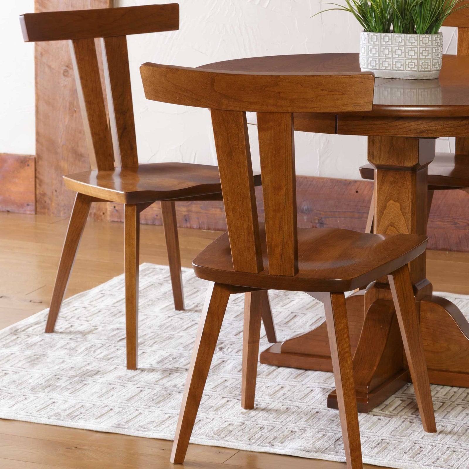 Two mid century modern cherry dining chairs with T-shaped crest rails and saddle seats at a round pedestal table