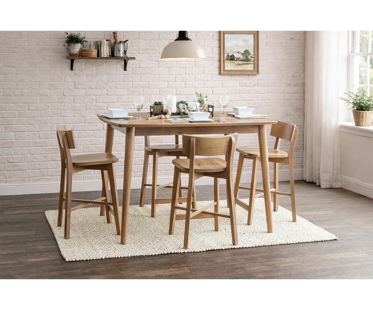 Oak counter height table with four curved-back stools, place settings and greenery in a white brick dining nook
