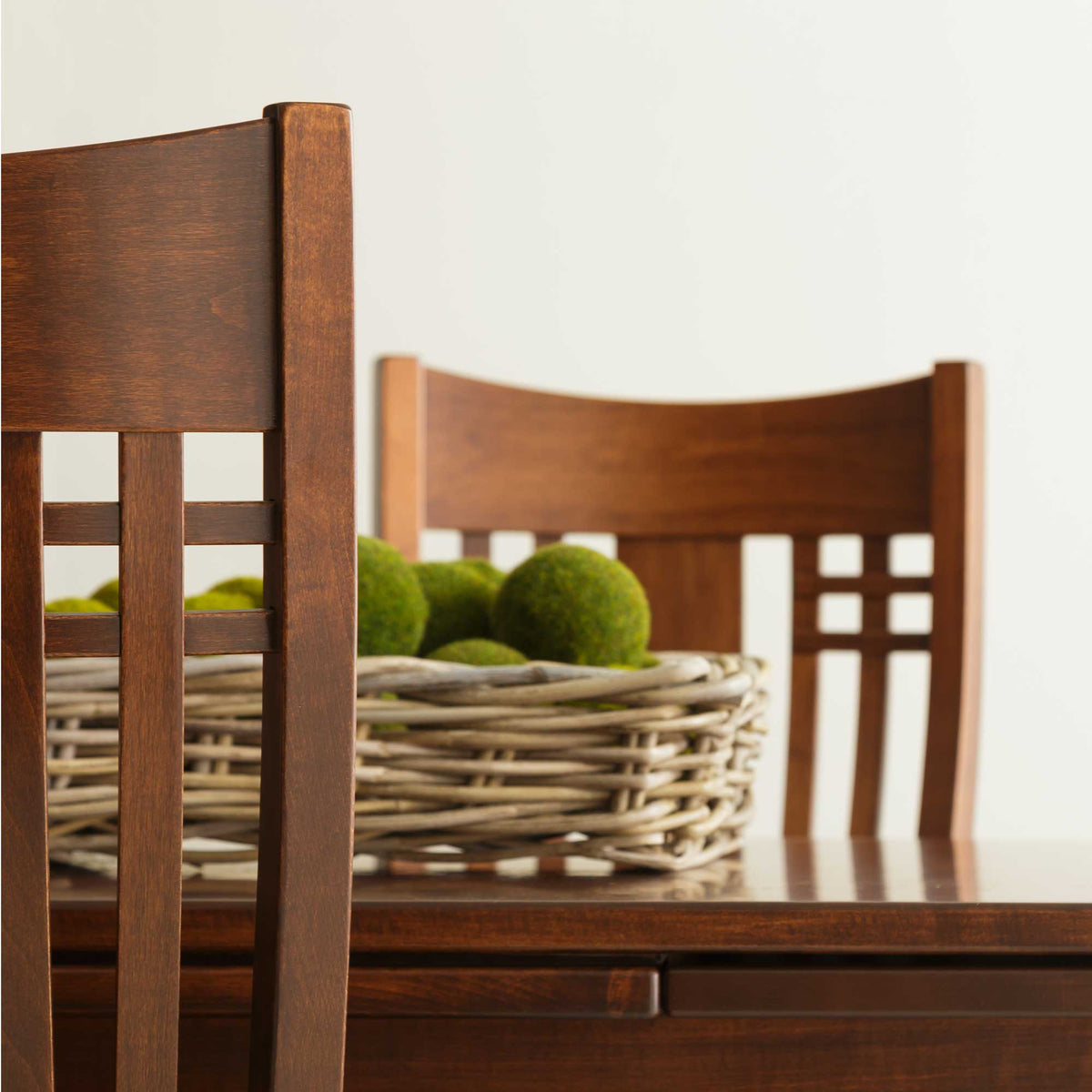 Close view of two cherry chair backs with square lattice cutouts beside a basket of green moss balls