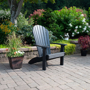 Black poly Adirondack chair with fanned slat back and wide arms on a paver patio surrounded by flowering shrubs