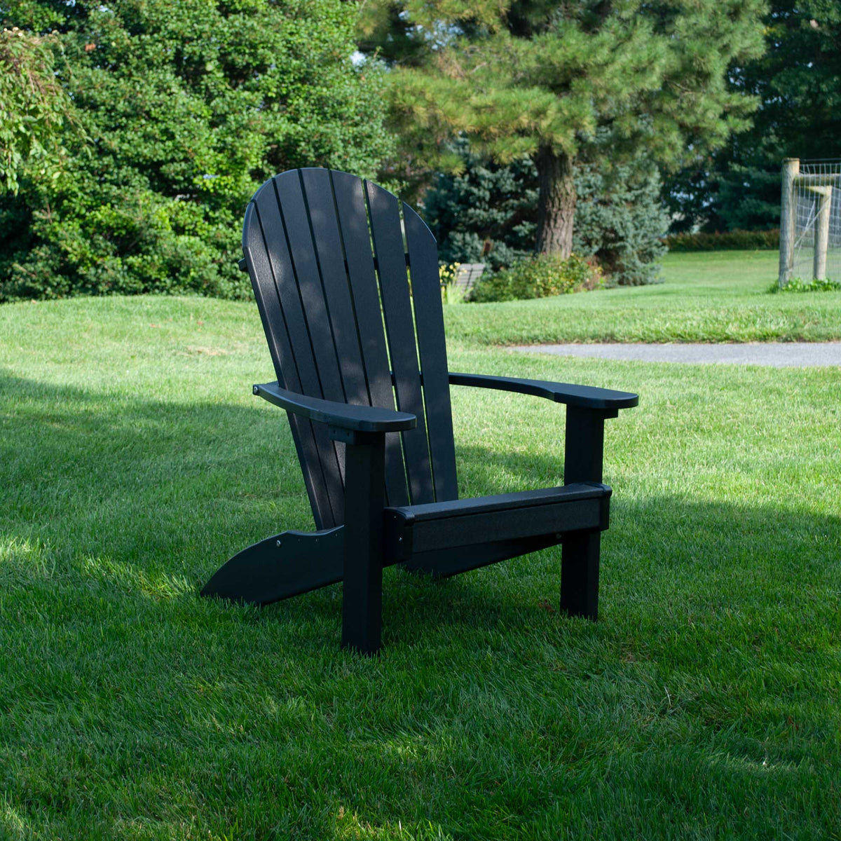 Black poly Adirondack chair with contoured slat back and flat arms sitting on a green lawn near evergreens