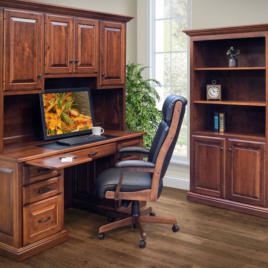 Black leather executive desk chair with channeled back and wood arms beside a cherry desk with hutch