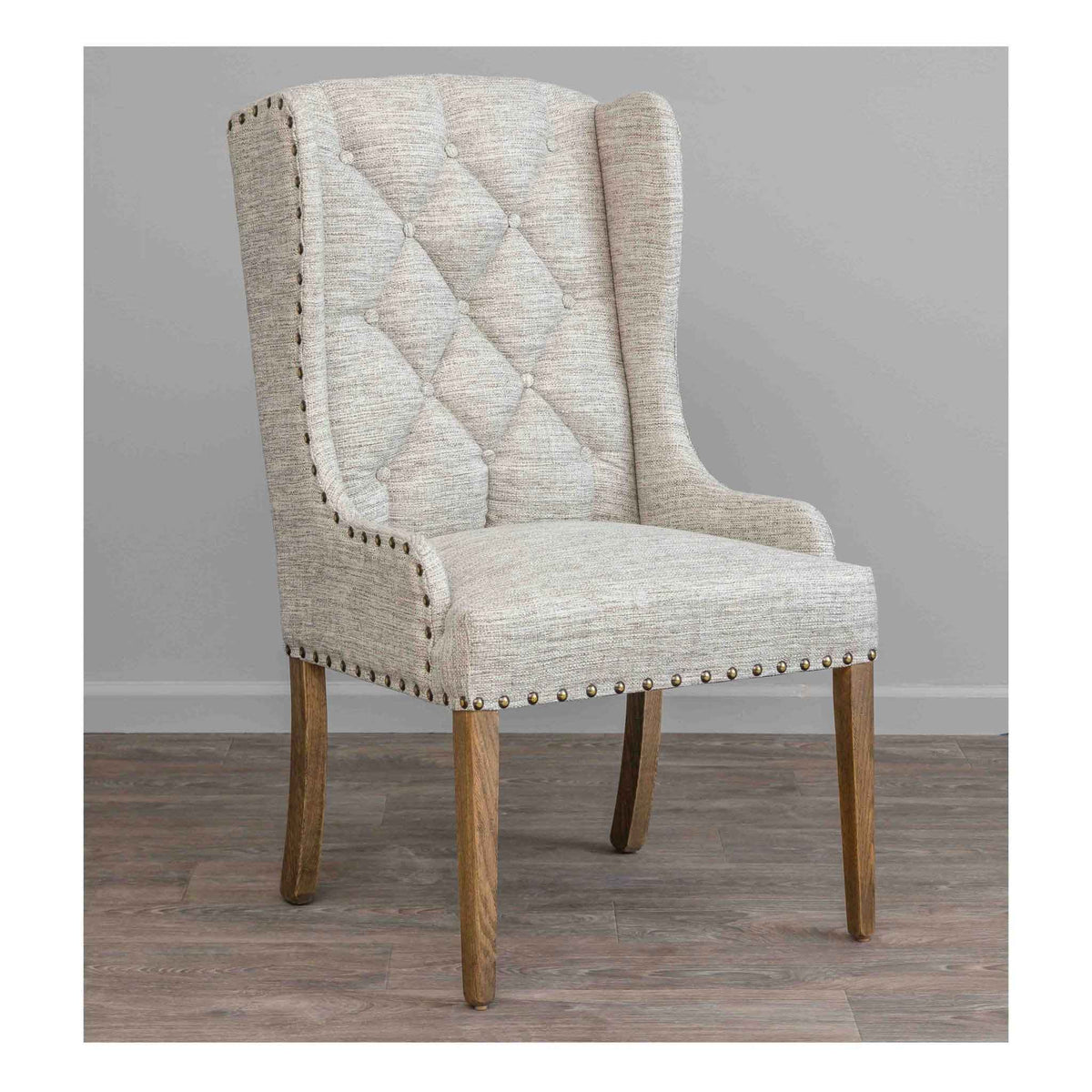 Tufted wingback dining chair in a natural flax weave with brass nailhead outline and driftwood oak tapered legs