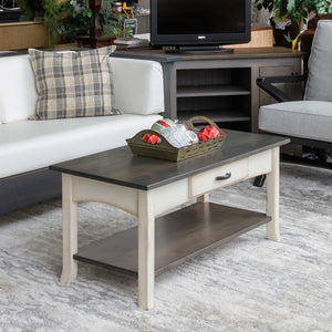 Two-tone coastal coffee table with a weathered gray top, cream painted base, drawer and lower shelf in a living room