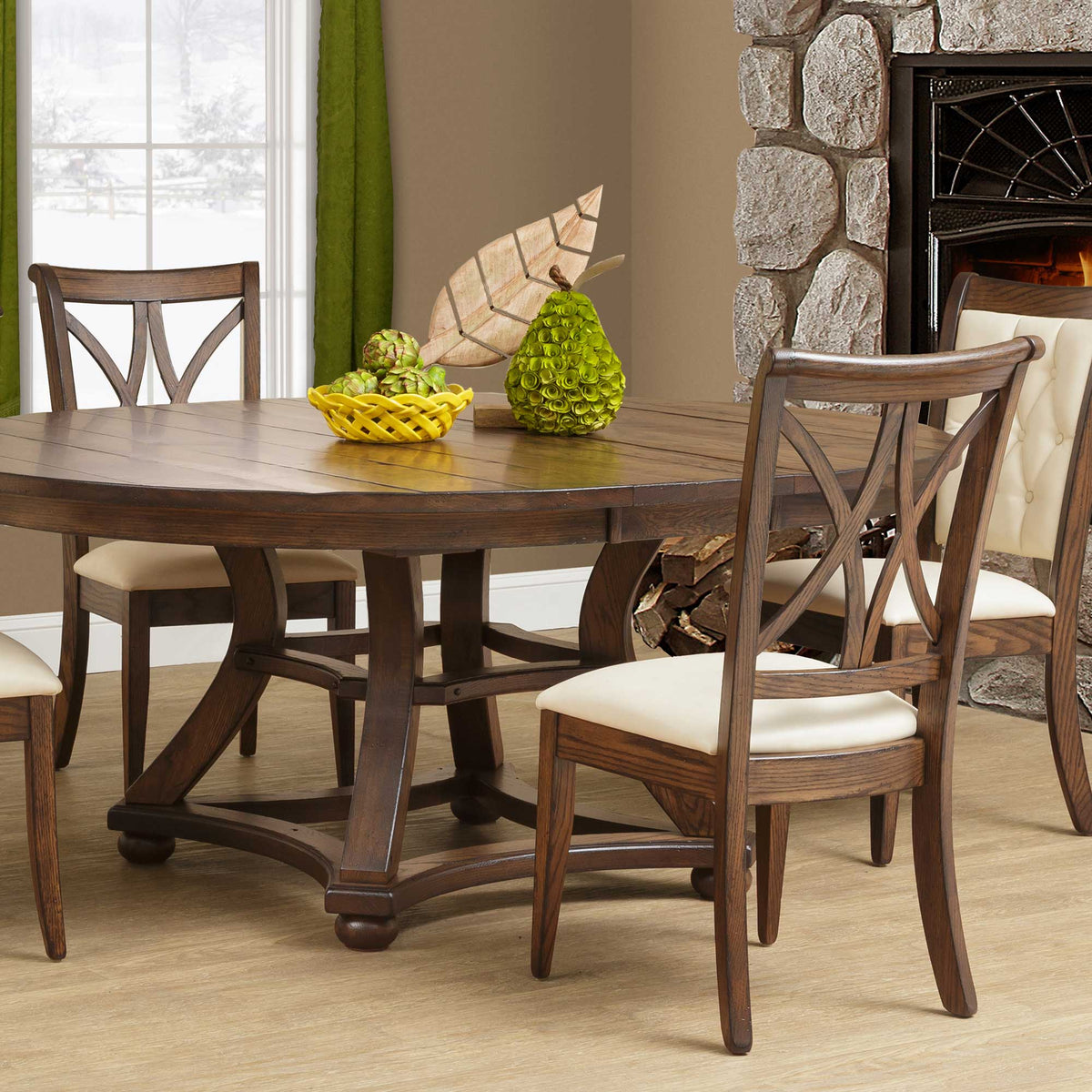 X back dining side chairs in weathered oak with cream upholstered seats around a round pedestal table by a stone fireplace