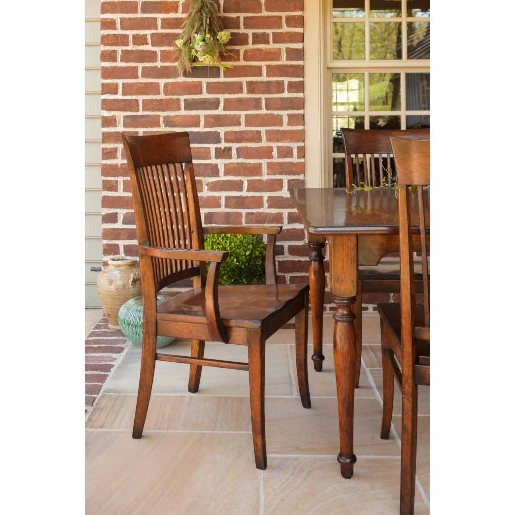 Cherry slat back dining chairs with solid wood seats around a turned leg farmhouse table by a brick wall