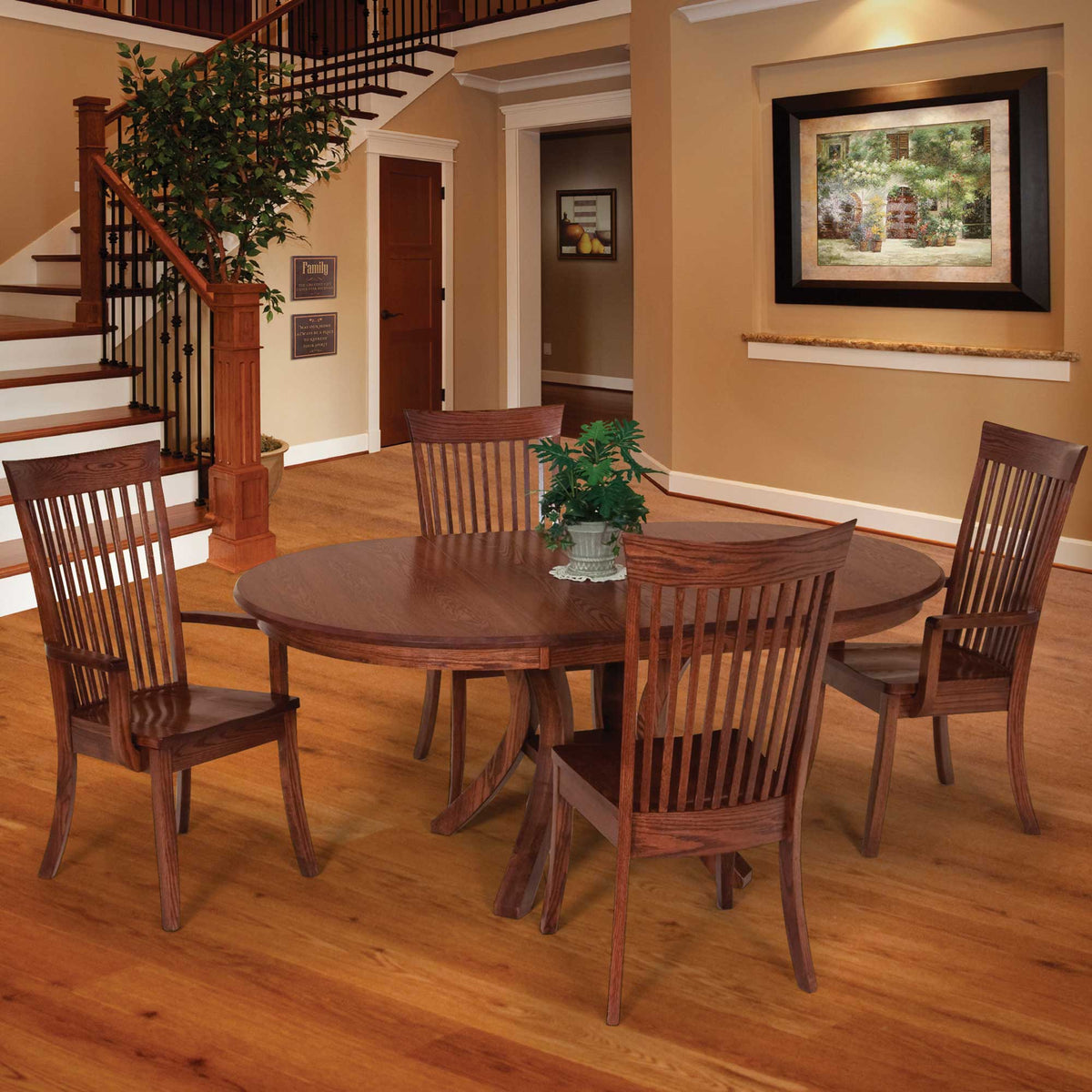 Round oak pedestal dining table with four tall slat back chairs in a warm entry hall with hardwood floors