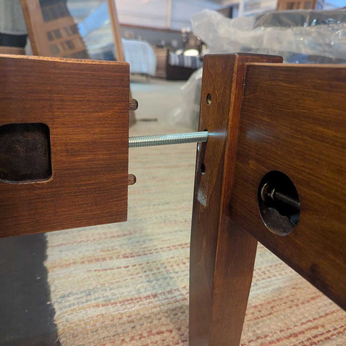 Bed rail joinery detail with a threaded bolt connecting the side rail to a tapered post of a stained wood bed