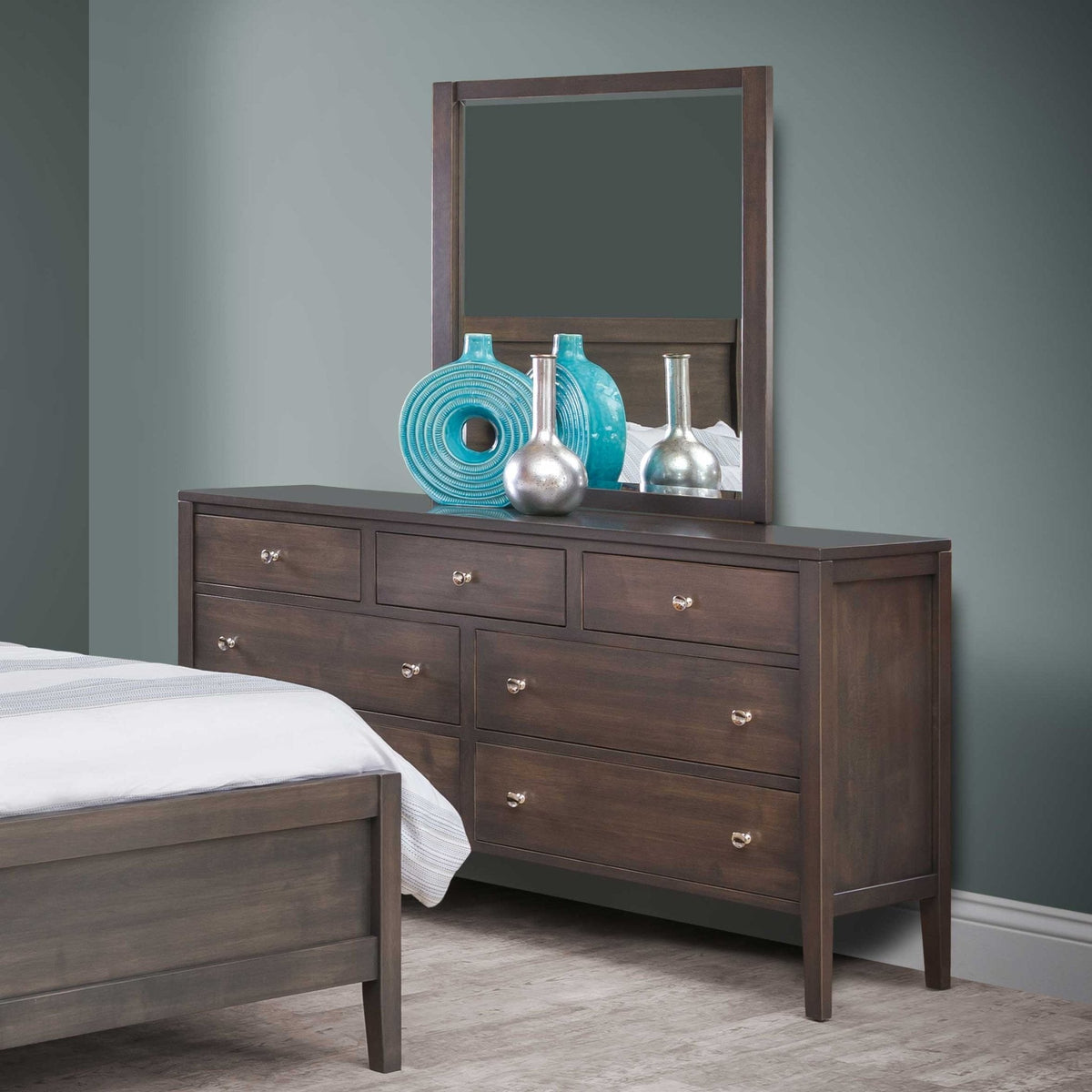 Dark gray dresser topped with a mirror and turquoise vases beside a matching bed in a teal painted bedroom