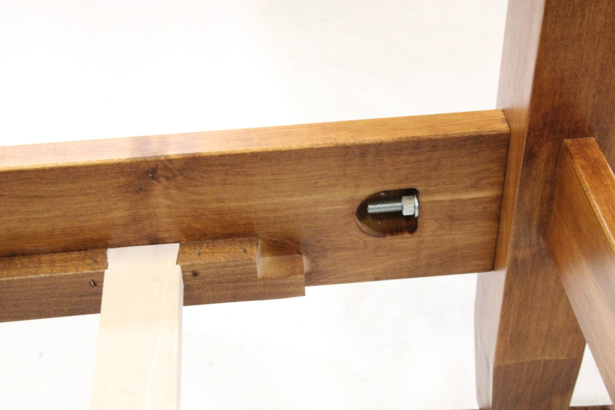 Close-up of a bed side rail with a countersigned bolt fastener and slat support ledge in warm brown wood