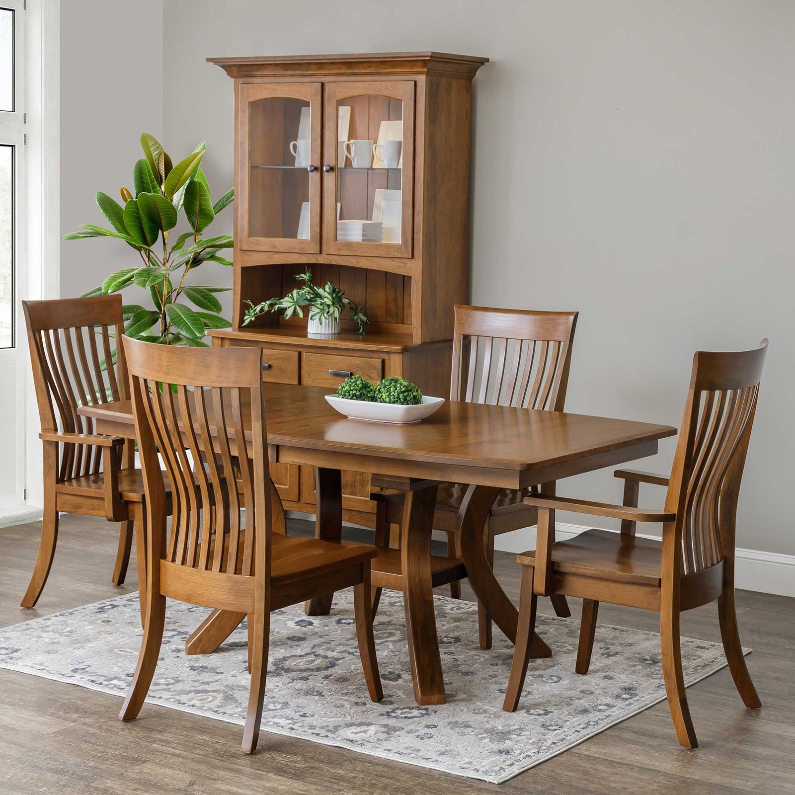 Brown maple expandable pedestal dining table with four curved slat back chairs and a matching corner china cabinet