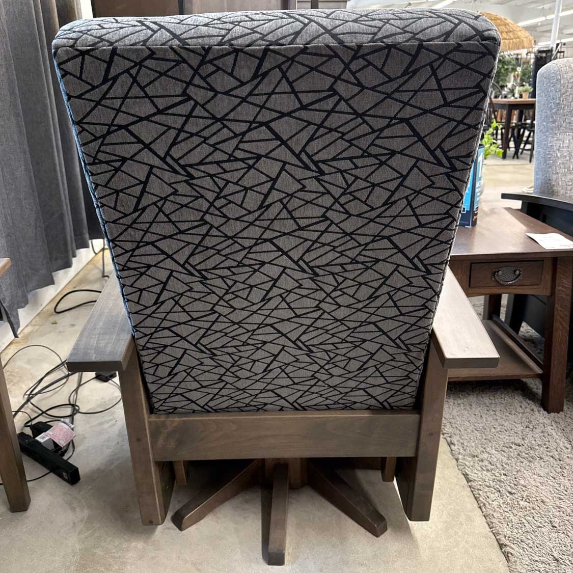 Rear view of a gray patterned swivel glider on a showroom floor with the paneled base and swivel post visible