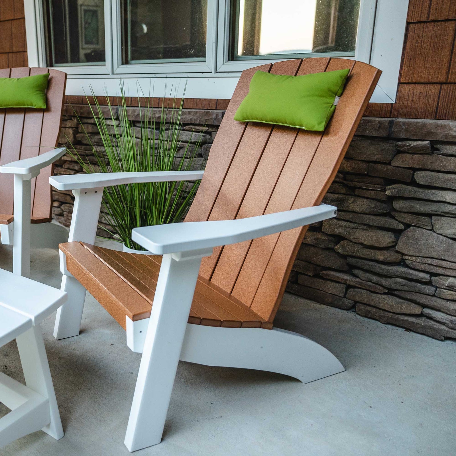 Two antique mahogany poly Adirondack chairs with squared modern arms in front of a white house with hostas