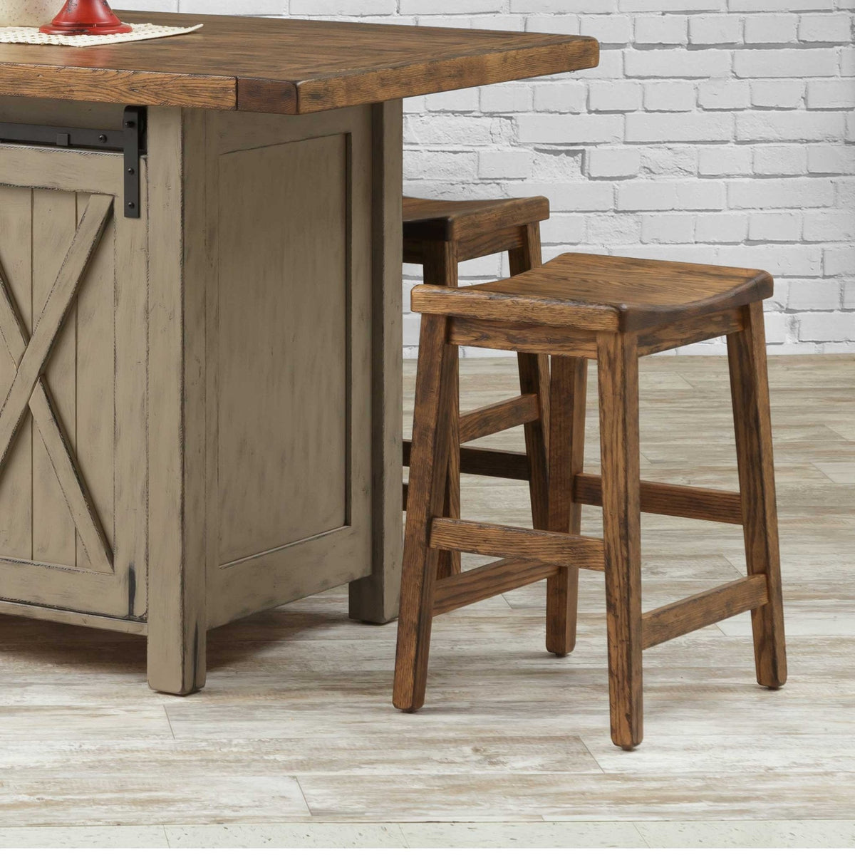 Two rustic oak saddle seat counter stools pulled up to a gray barn door kitchen island against white brick