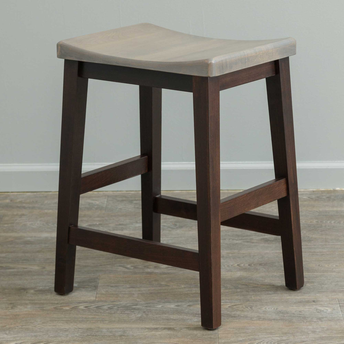 Two-tone counter stool with a driftwood gray saddle seat and dark brown legs with H stretcher footrests