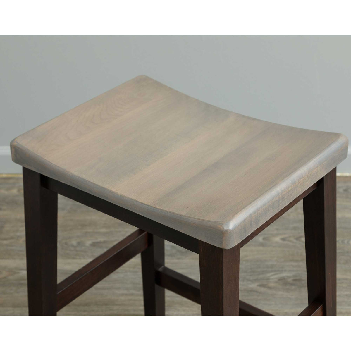 Close-up of the scooped gray saddle stool seat showing wood grain and rounded edges over dark tapered legs