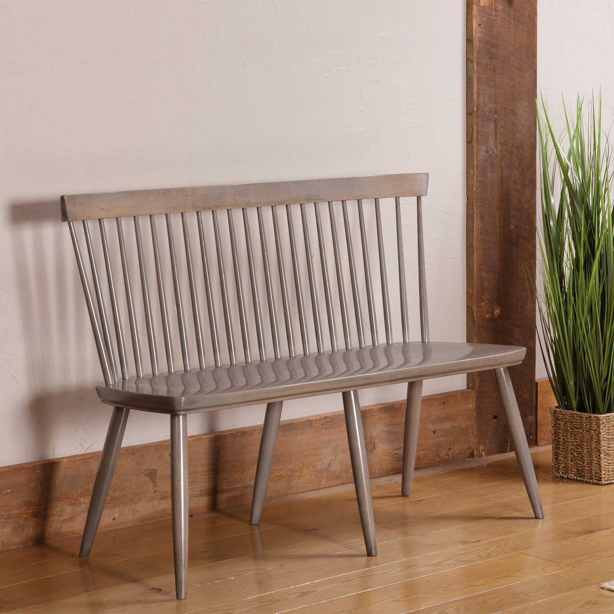 Weathered gray Windsor spindle bench with a shaped plank seat and angled tapered legs against a white wall