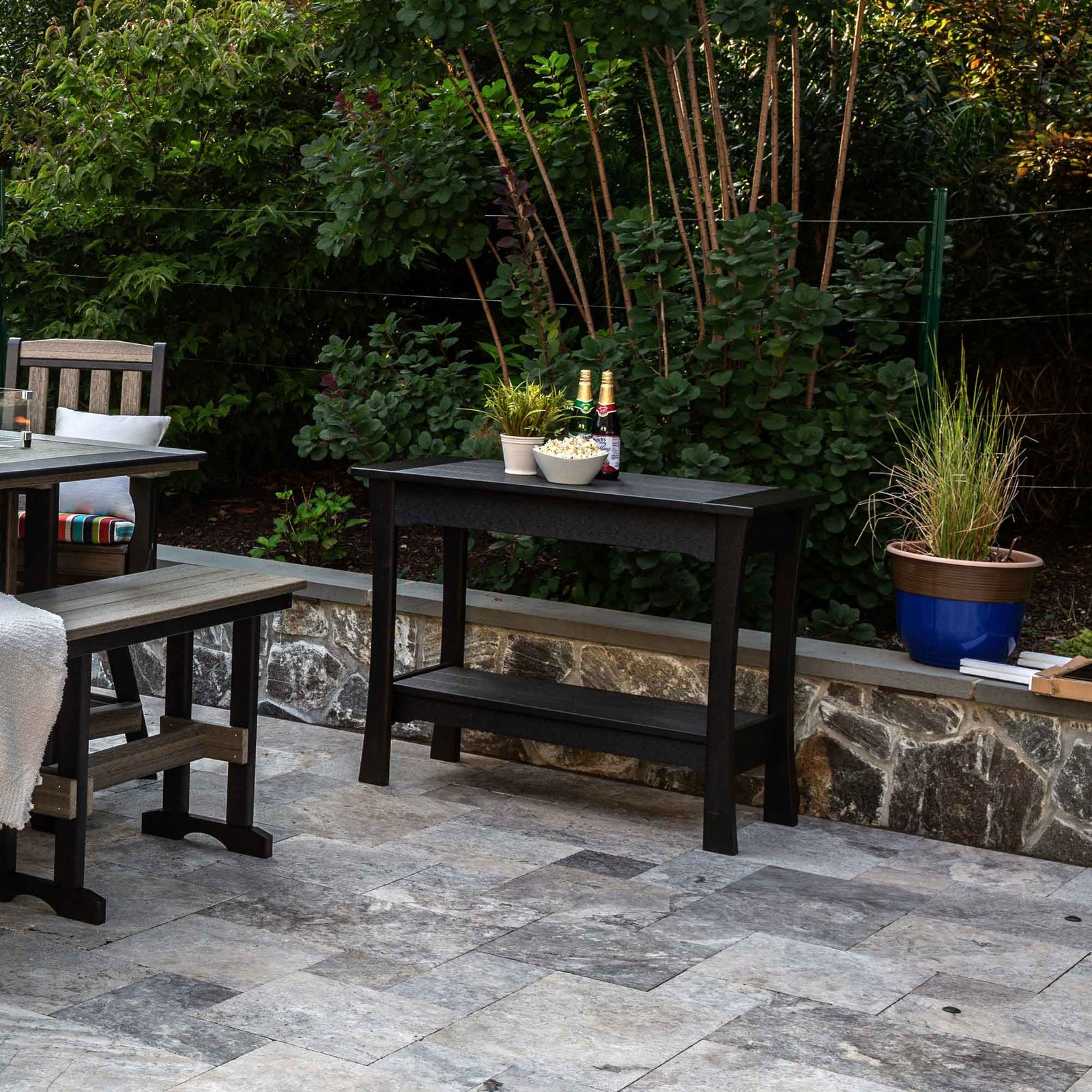 Black poly patio bar serving table with a rectangular top and lower shelf holding snacks and drinks