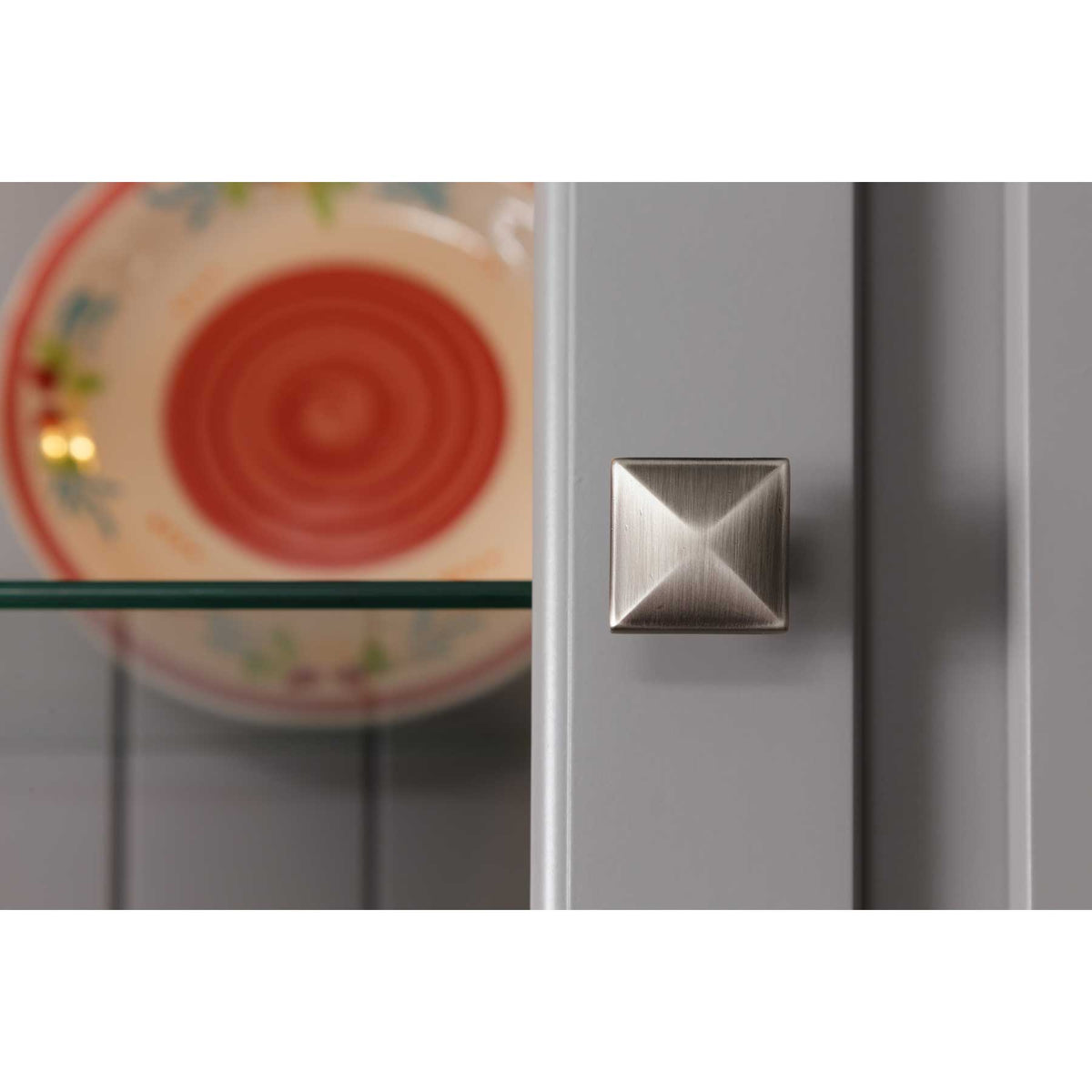 Close-up of a brushed nickel square knob on the gray hutch glass door with a plate on the glass shelf