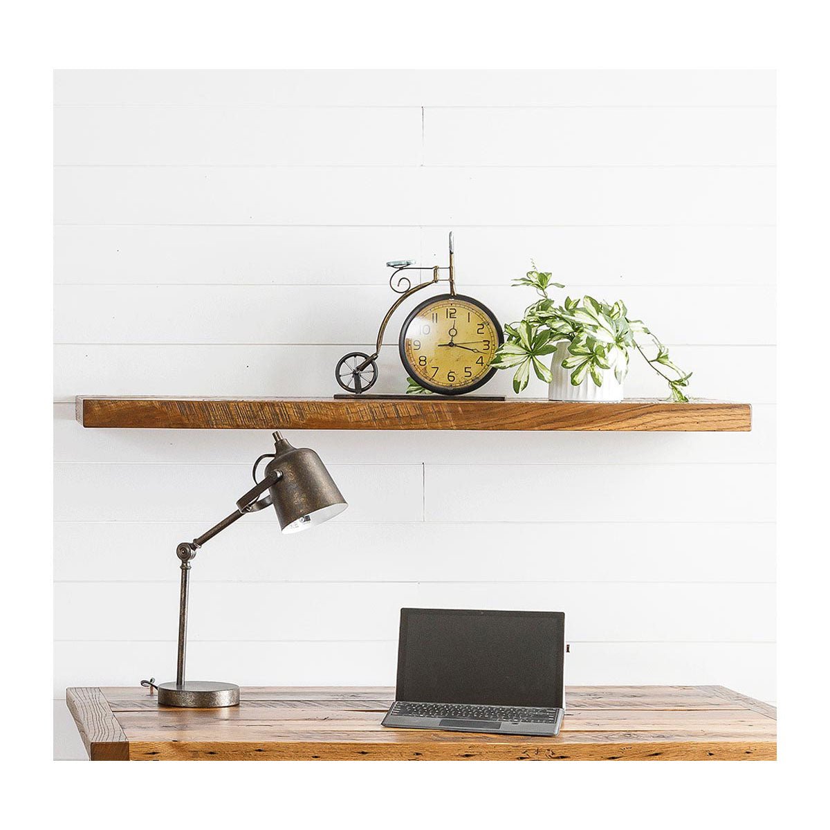Reclaimed wood floating shelf mounted on white shiplap, holding a vintage clock and small plant above a desk
