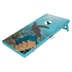 Teal framed cornhole board printed with a sea turtle over coral reef, teal and tan bean bags on the surface