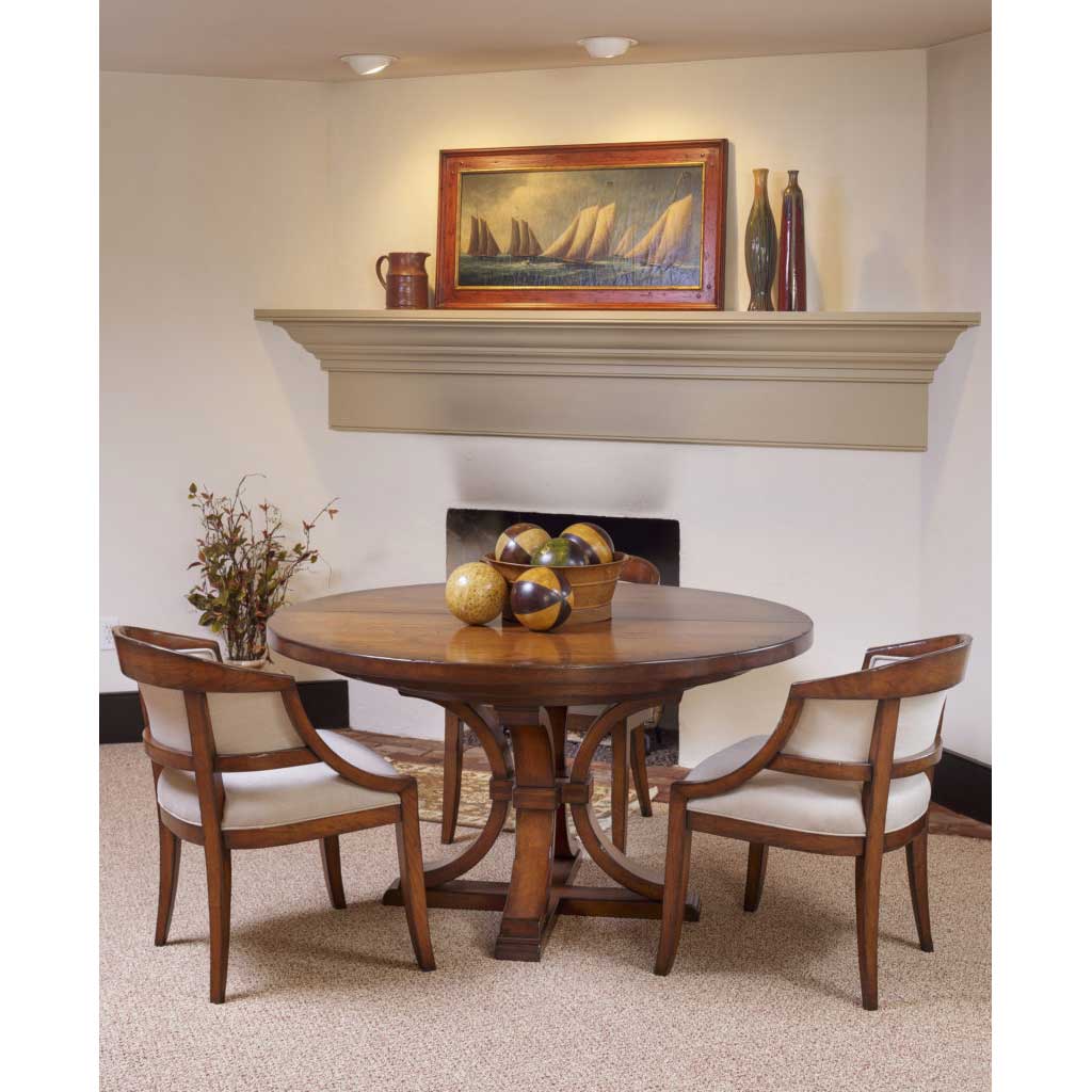 Round pedestal dining table in cherry with two upholstered barrel arm chairs in front of a fireplace