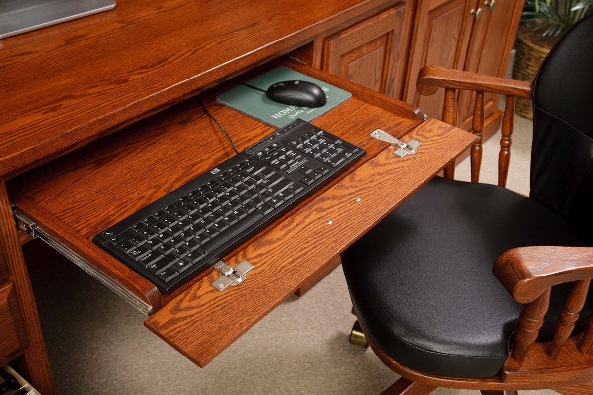 Oak keyboard tray extended below the desk top with keyboard and mouse pad, beside a leather office chair